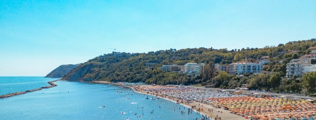 Spiaggia affollata con ombrelloni colorati e mare calmo.