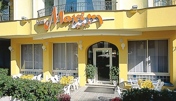 Facciata gialla dell'hotel con tavoli esterni.