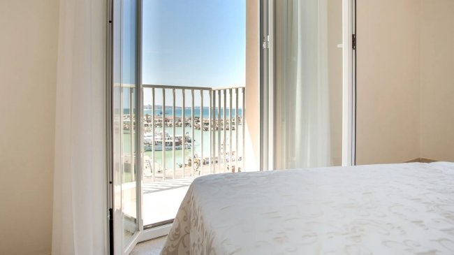 Vista marina da porta-finestra con letto bianco.