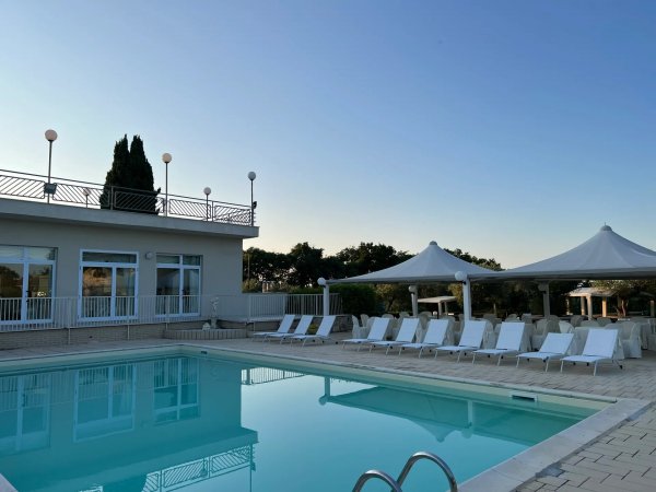 Piscina all'aperto con lettini e tettoia bianca.