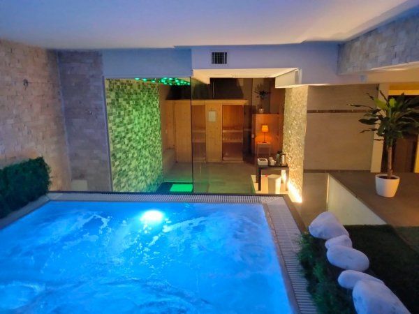 Interno con piscina illuminata e sauna sullo sfondo.