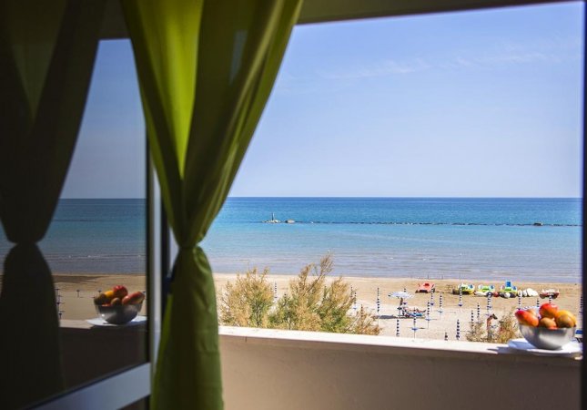 Vista mare da finestra con tende verdi.