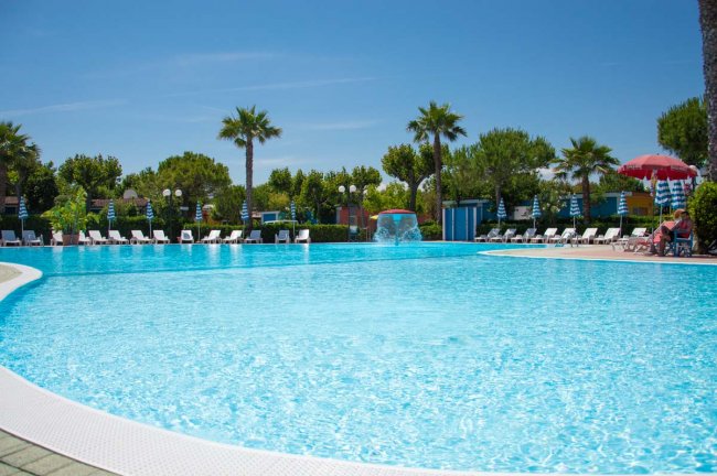 Piscina all'aperto con lettini e palme.
