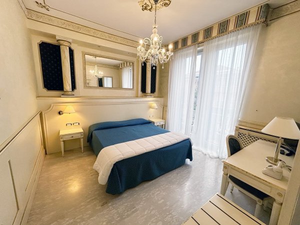 Camera con letto blu, lampadario e tende chiare.