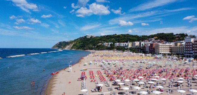 Spiaggia con ombrelloni colorati e mare, edifici sullo sfondo.