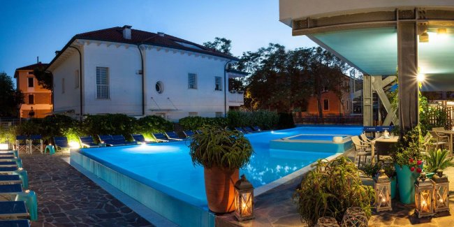 Piscina illuminata con sedie a sdraio e lanterne.