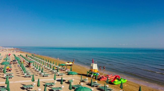 Spiaggia con file di ombrelloni verdi.