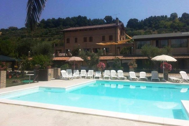 Piscina con lettini e ombrelloni, edificio sullo sfondo.
