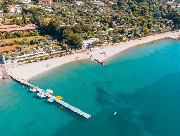 Spiaggia con molo e barche, viste dall'alto, acqua turchese e costa alberata.