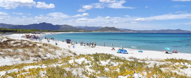 Spiaggia bianca con mare blu e persone in lontananza.