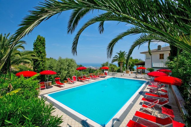 Piscina all'aperto con sdraio e ombrelloni rossi.