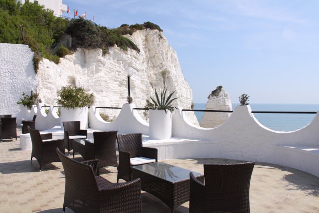 Terrazza con sedie e vista su scogli bianchi.