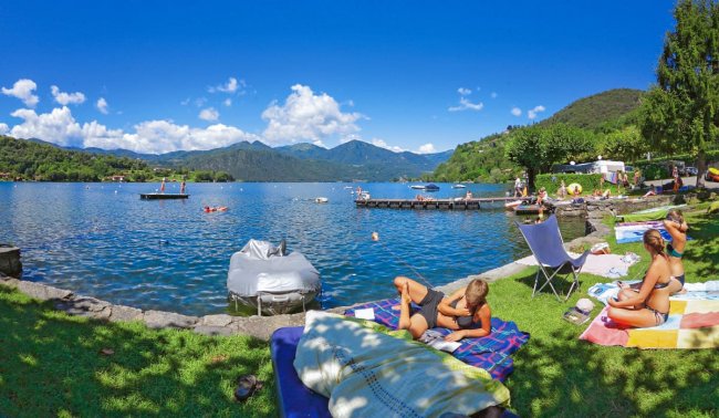 Persone rilassate su un prato, fronte lago e montagne.
