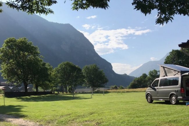 Furgone in un prato con montagne e alberi.