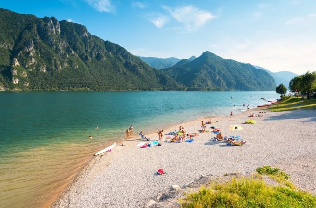 Spiaggia di ciottoli e lago con montagne.
