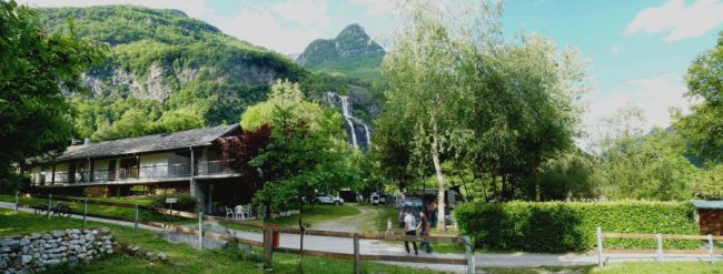 Una casa rustica circondata da alberi e una cascata in lontananza.