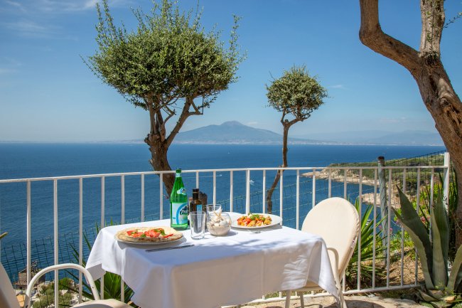 Tavolo all'aperto con vista mare e piatti serviti.