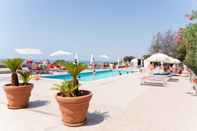 Piscina con lettini e ombrelloni in un terrazzo vista mare.