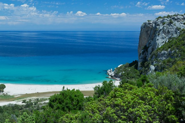Spiaggia e mare turchese, scogliera sul lato destro.