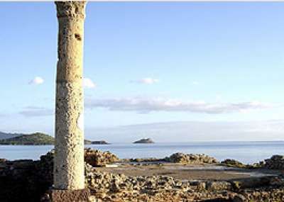 Rovine di una colonna davanti a un paesaggio marino con isole in lontananza.