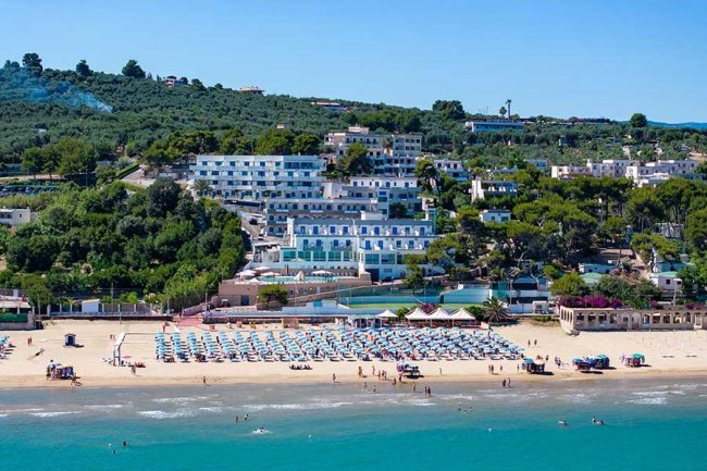 Spiaggia affollata con ombrelloni, mare e colline sullo sfondo.