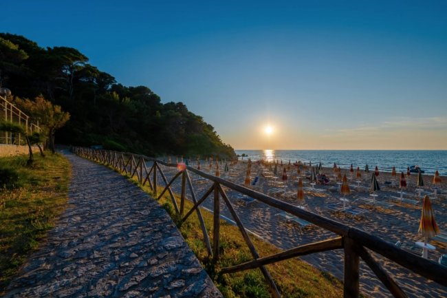 Sentiero costiero al tramonto, con spiaggia e ombrelloni.
