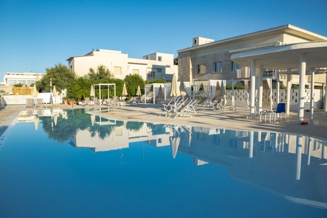 Ampia piscina con lettini e ombrelloni bianchi.
