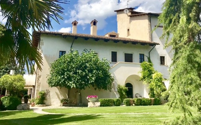 Villa storica con giardino e alberi verdi.
