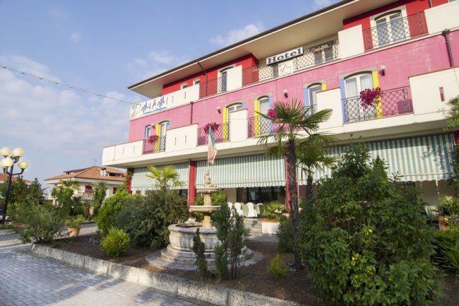 Facciata di un hotel rosa con balconi e giardino.