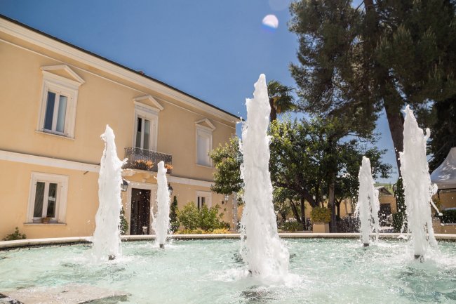 Fontana con zampilli e un edificio giallo sullo sfondo.