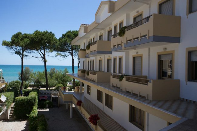 Edificio a più piani con balconi, vista mare e alberi sullo sfondo.