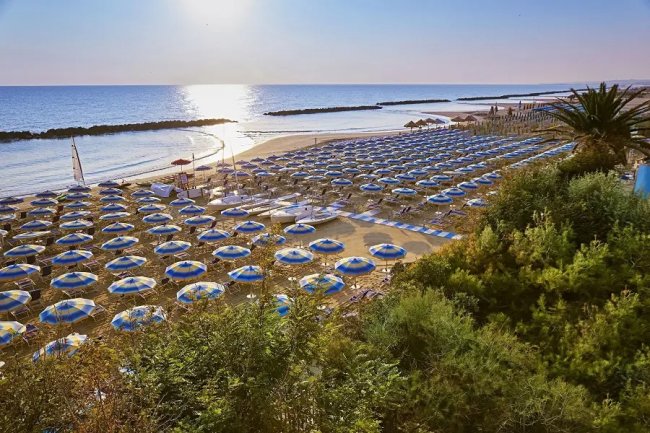 Spiaggia con ombrelloni blu e mare al tramonto.