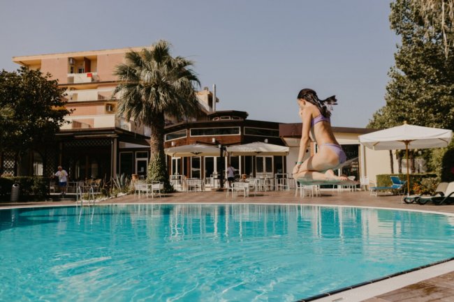 Donna che salta in piscina, edificio e palme sullo sfondo.