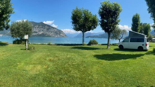 Camper su prato verde con vista lago e montagne.