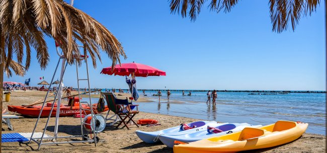 Kayak colorati su una spiaggia con ombrellone rosso.