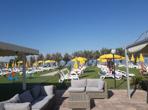 Spiaggia con lettini, ombrelloni gialli e divani.