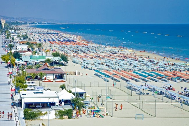 Spiaggia affollata con lettini e ombrelloni lungo il mare.