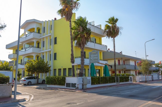 Hotel giallo con balconi e palme.