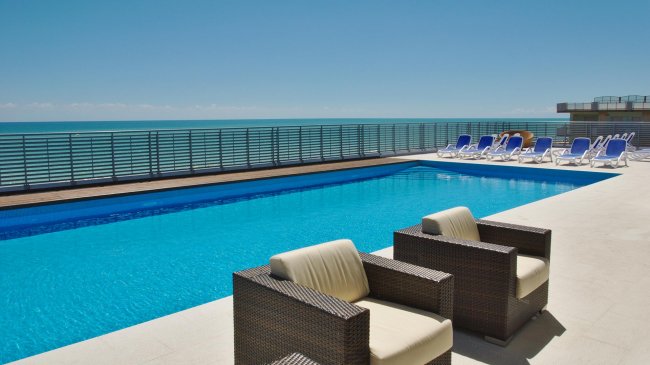 Piscina blu con sedie a sdraio e poltrone.
