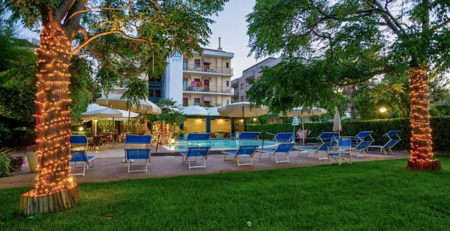 Albergo con piscina e sedie a sdraio, albero illuminato.