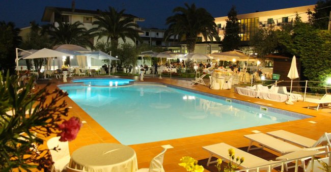 Piscina illuminata di notte con tavoli per eventi.