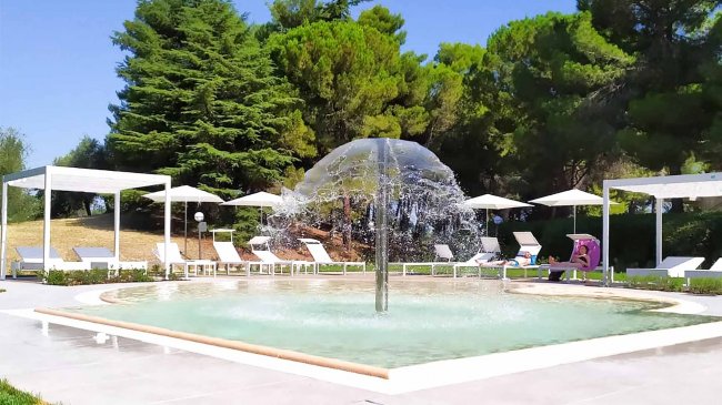 Fontana centrale in una piscina con sdraio intorno.