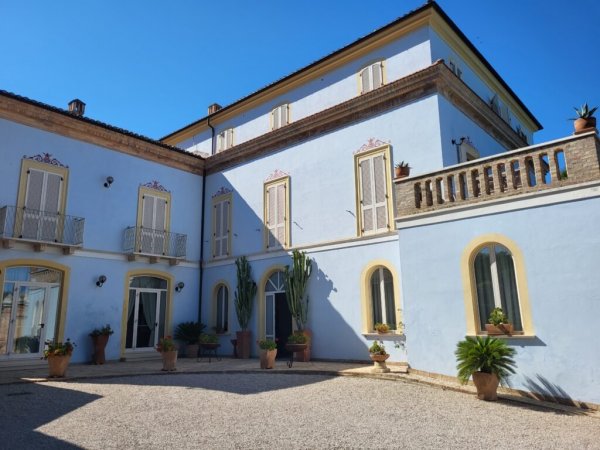 Edificio storico azzurro con cortile e piante.
