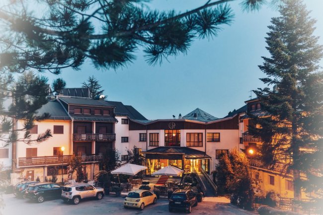 Hotel di montagna con luci accese, circondato da alberi.