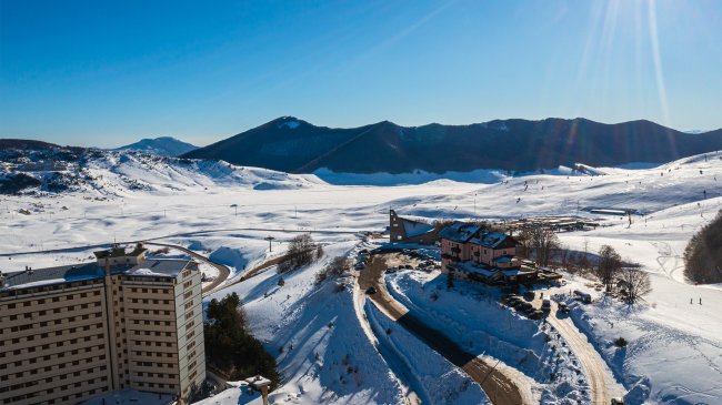Paesaggio innevato con edifici e montagne in lontananza.