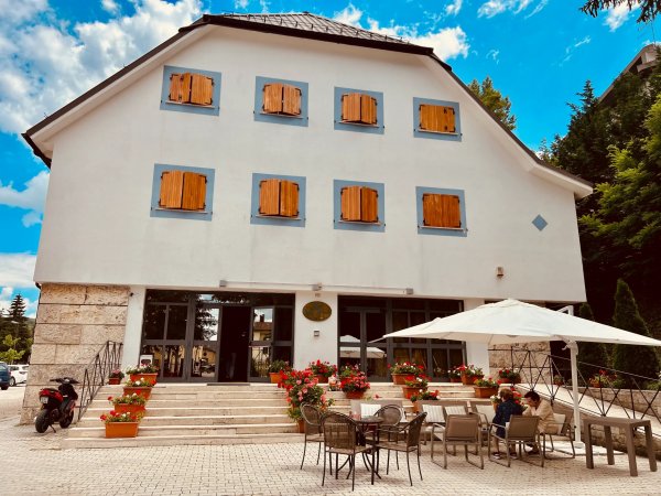Edificio bianco con finestre in legno e tavoli all'esterno.