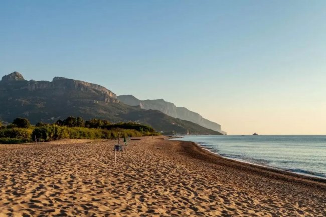 Spiaggia sabbiosa con montagne sullo sfondo.