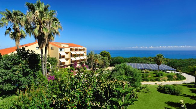 Edificio giallo con palme e giardino.