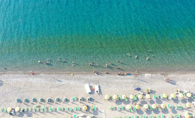 Vista aerea di una spiaggia con lettini e mare blu.