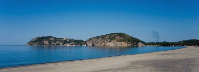 Una spiaggia sabbiosa con mare calmo e colline sullo sfondo.